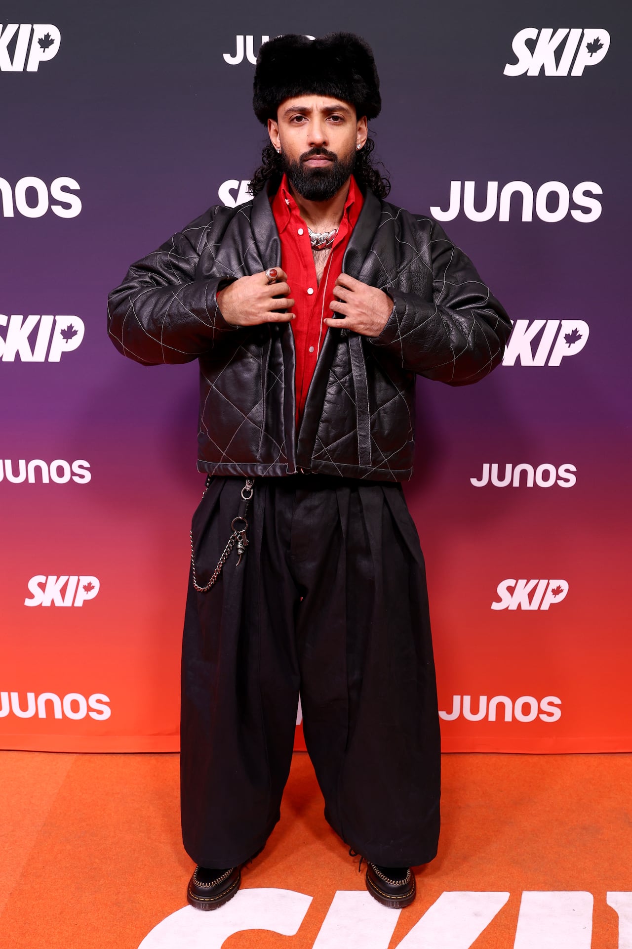 A man takes pictures wearing black pants, a leather jacket and a fur hat.