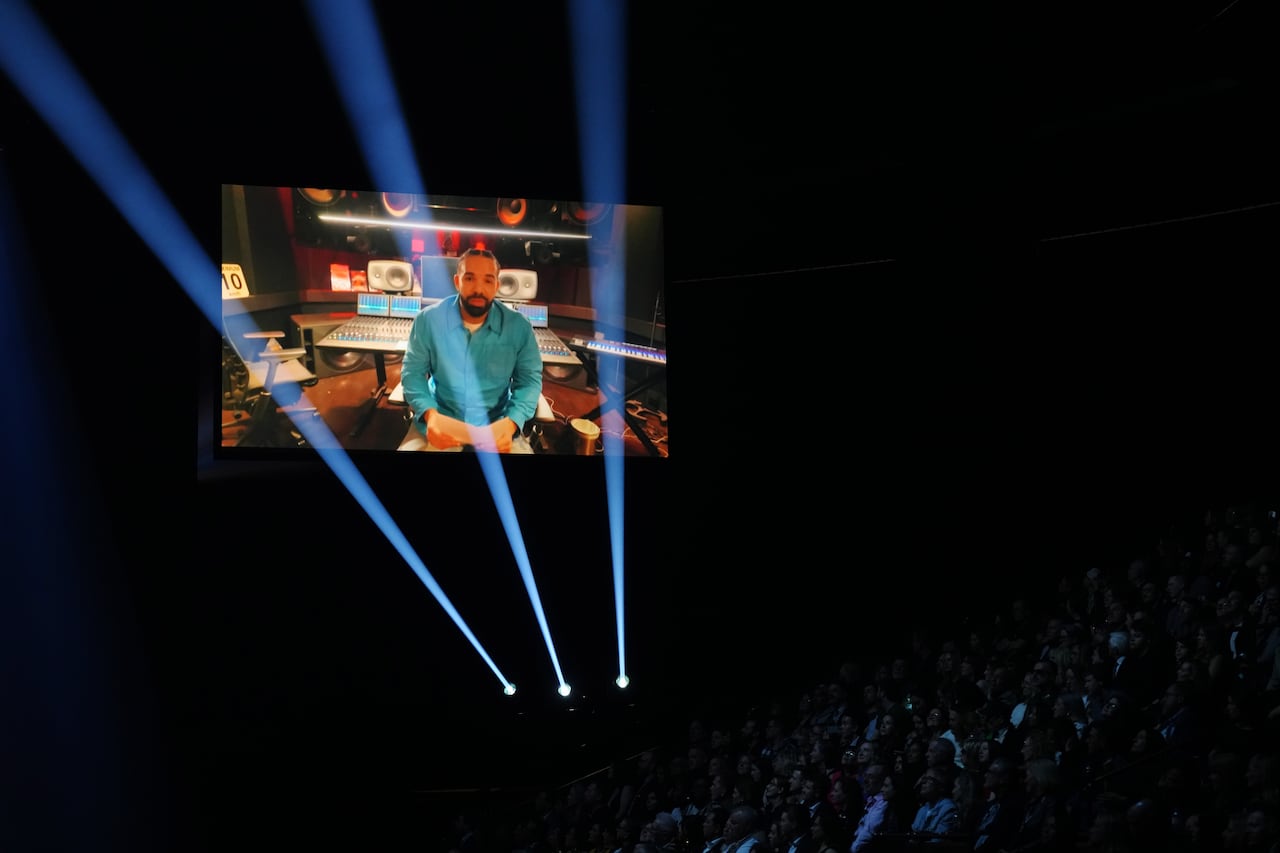 The man on the screen is seen above the crowd in the dark.