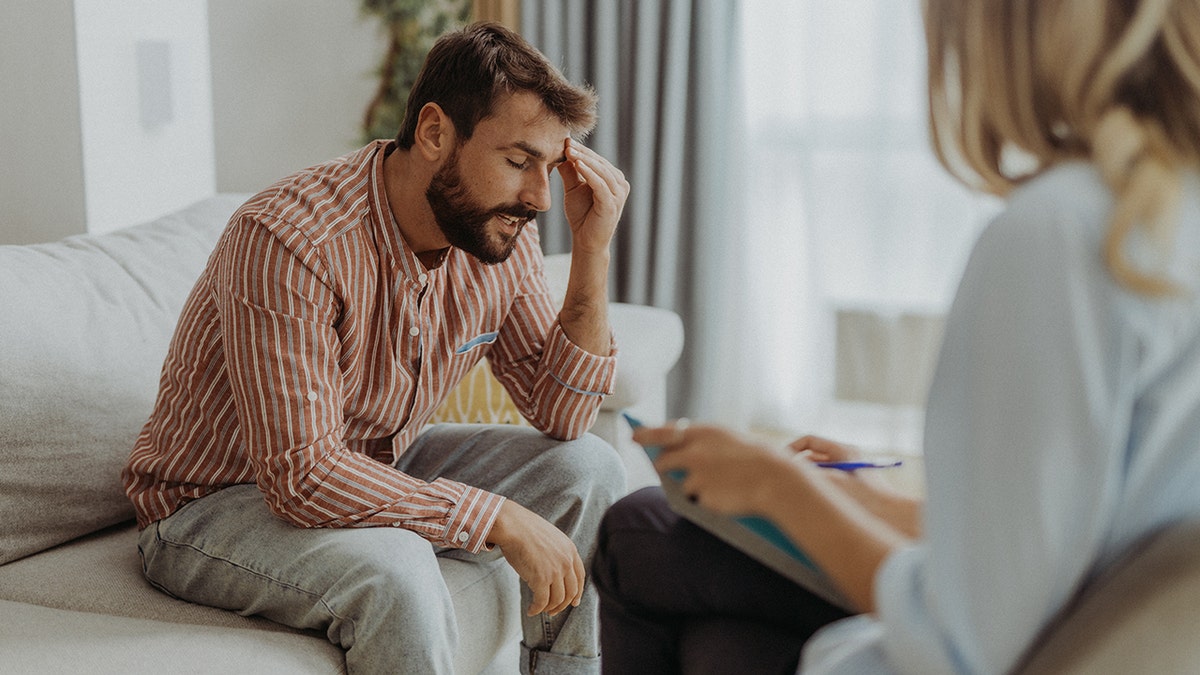 a man is sitting on the couch with his hand on his forehead while talking to a female doctor